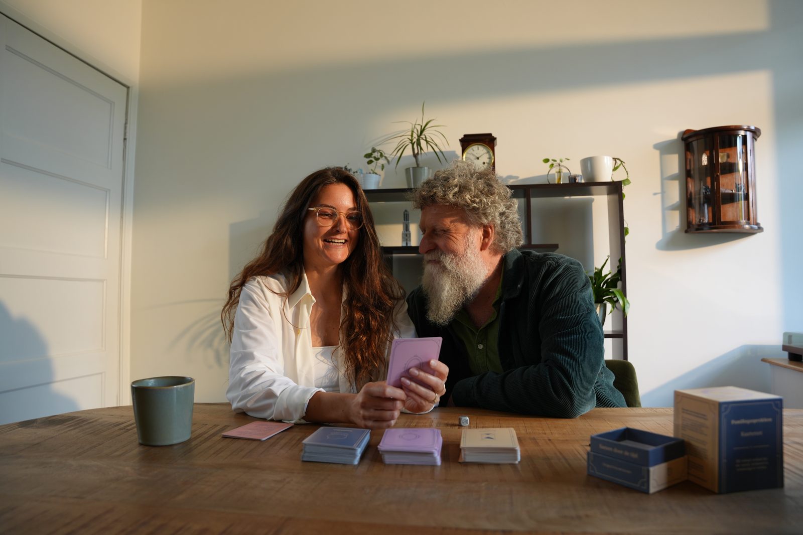 Vrouw en oudere man lachen samen tijdens het Familiegesprekken kaartspel aan tafel.