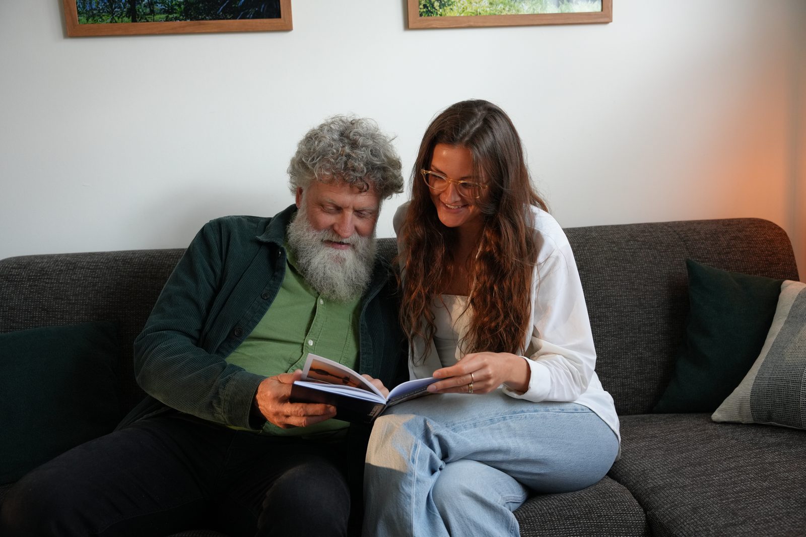 Een oudere en een jongere vrouw kijken samen glimlachend het levensboek door op de bank.